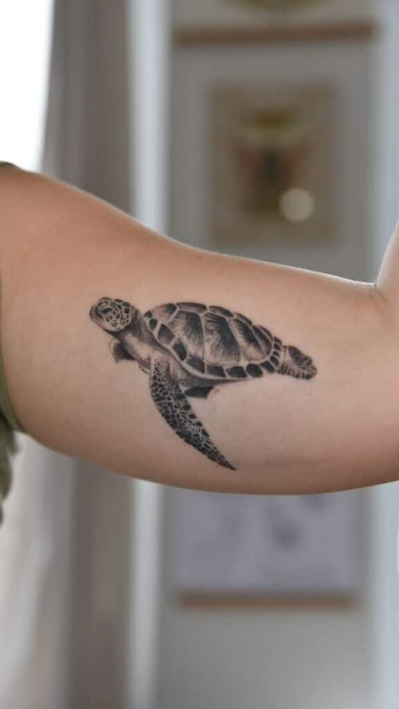 Sea turtle tattoo on upper arm, detailed black ink art, close-up view.