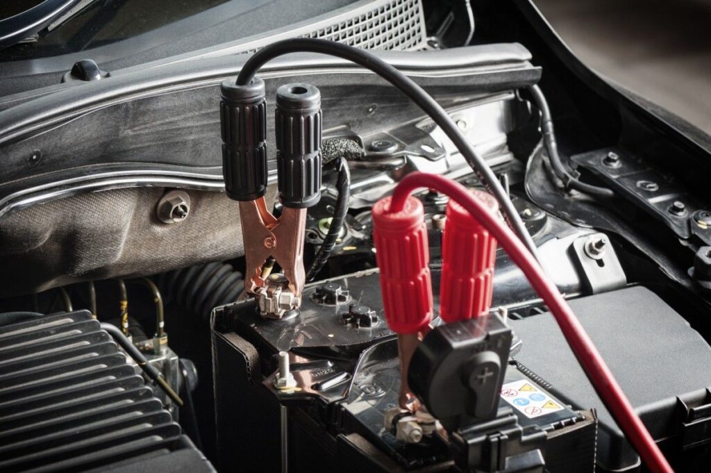 Car engine with jumper cables attached to battery terminals for jump-starting.