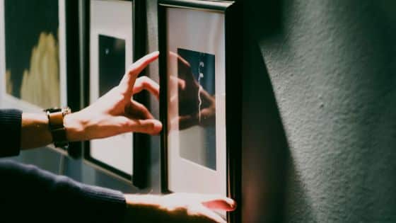 Person adjusting framed artwork on a wall, focusing on alignment and placement in a well-lit room.