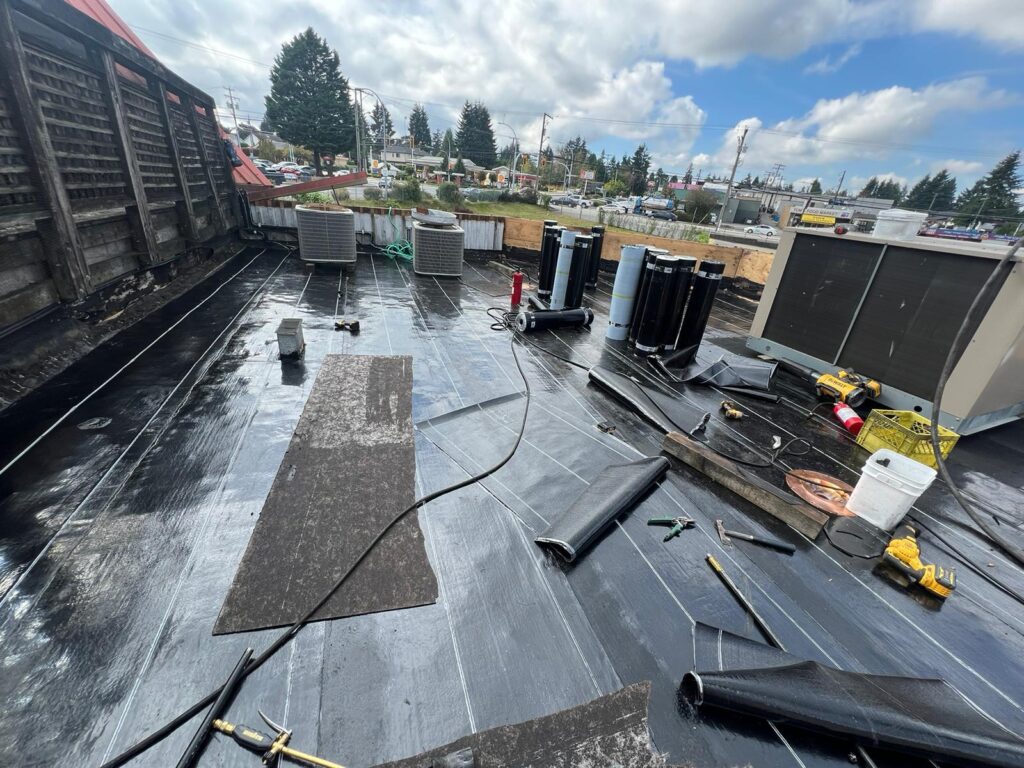 Roof construction site with roofing materials and tools under a cloudy sky.