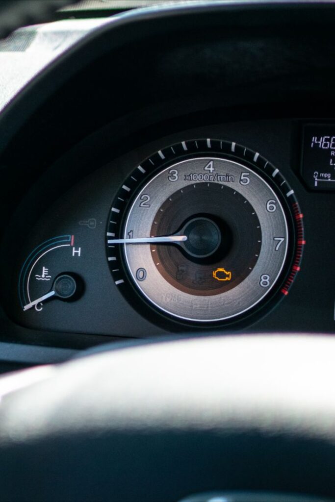 Car dashboard with illuminated check engine light and tachometer display.