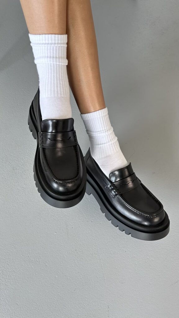 Black loafers paired with white socks on grey floor, showcasing modern style and comfort.