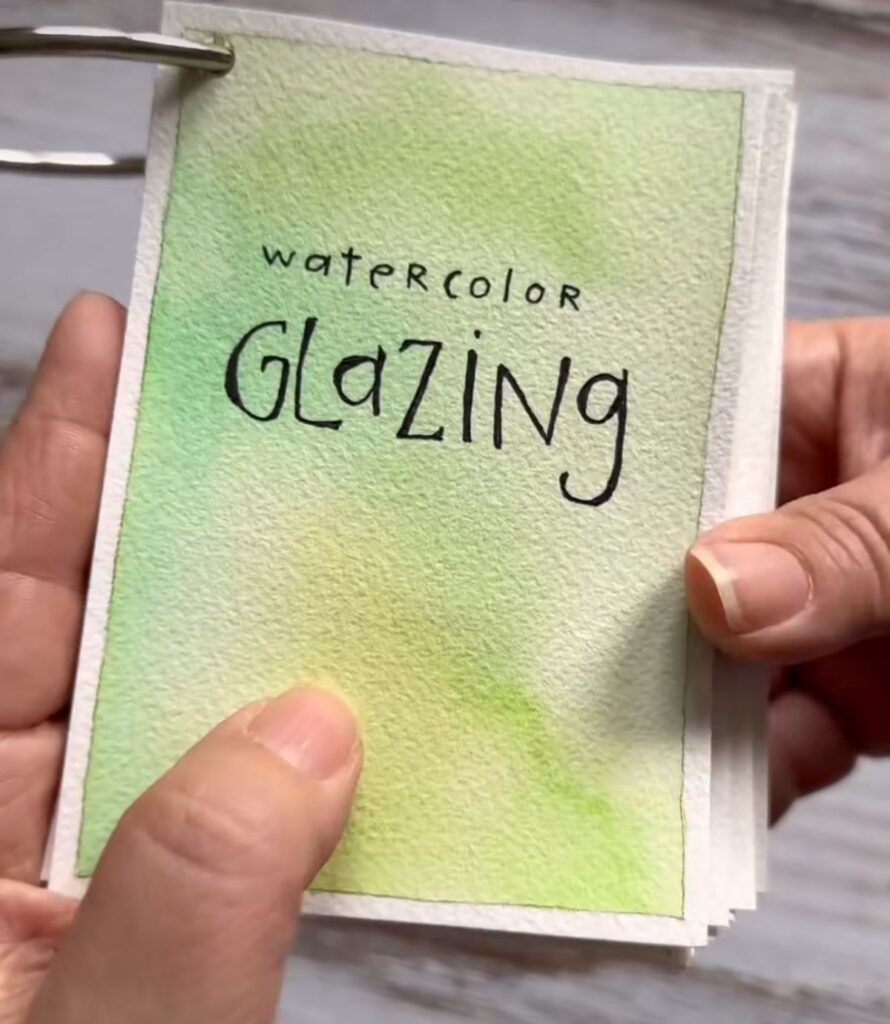 Watercolor glazing technique card with green gradient, held by hands.