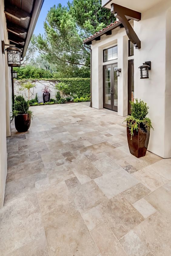 Elegant patio with stone tile flooring, potted plants, and double doors surrounded by lush greenery.