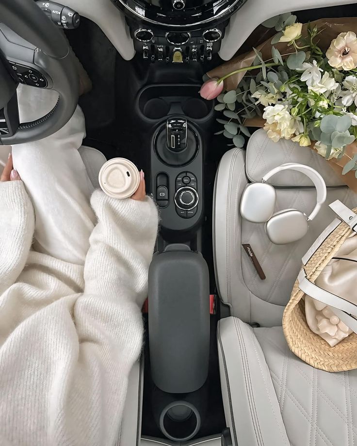 acfad895-17e1-4b5b-9ab6-6e03aeb6b346 Woman in cozy sweater holding coffee in car, with flowers, headphones, and straw bag on the seat. Light and stylish setup. | Sky Rye Design Woman in cozy sweater holding coffee in car, with flowers, headphones, and straw bag on the seat. Light and stylish setup.
