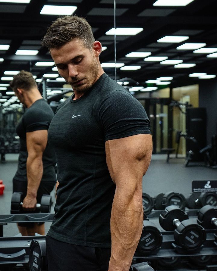 ae12ad61-f4d1-46f1-9d9a-4fd471d43c1a Man in black shirt lifting dumbbells in gym, focusing on strength training and fitness. | Sky Rye Design Man in black shirt lifting dumbbells in gym, focusing on strength training and fitness.