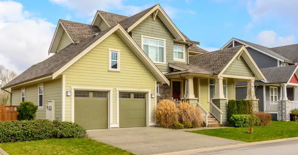 Modern suburban home with green siding, two-car garage, and manicured lawn under a blue sky.
