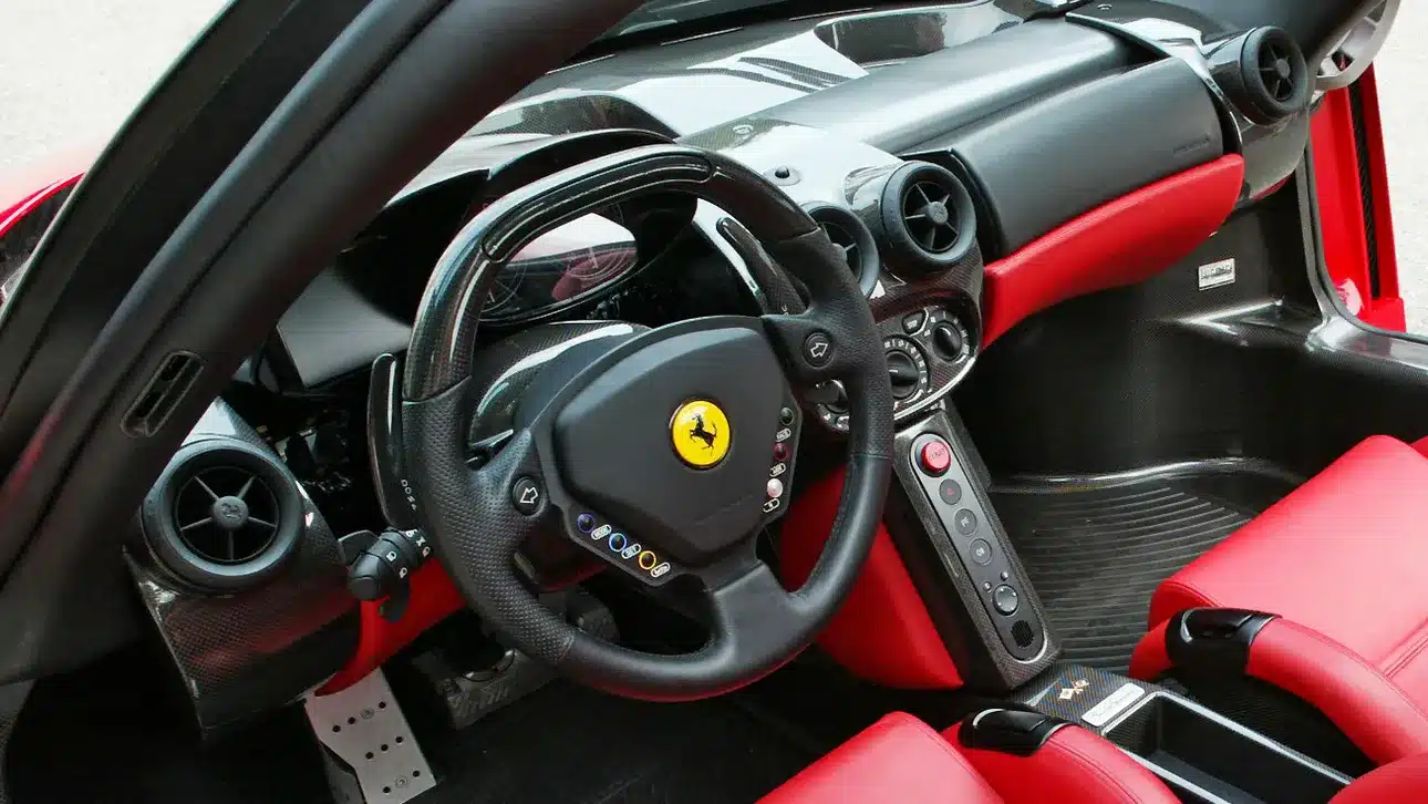 Close-up of a luxury sports car interior with red leather seats and a signature logo steering wheel.