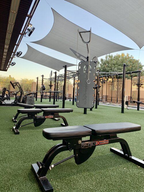 Outdoor gym with benches and fitness equipment on artificial grass under canopy shades. Perfect for open-air workouts.