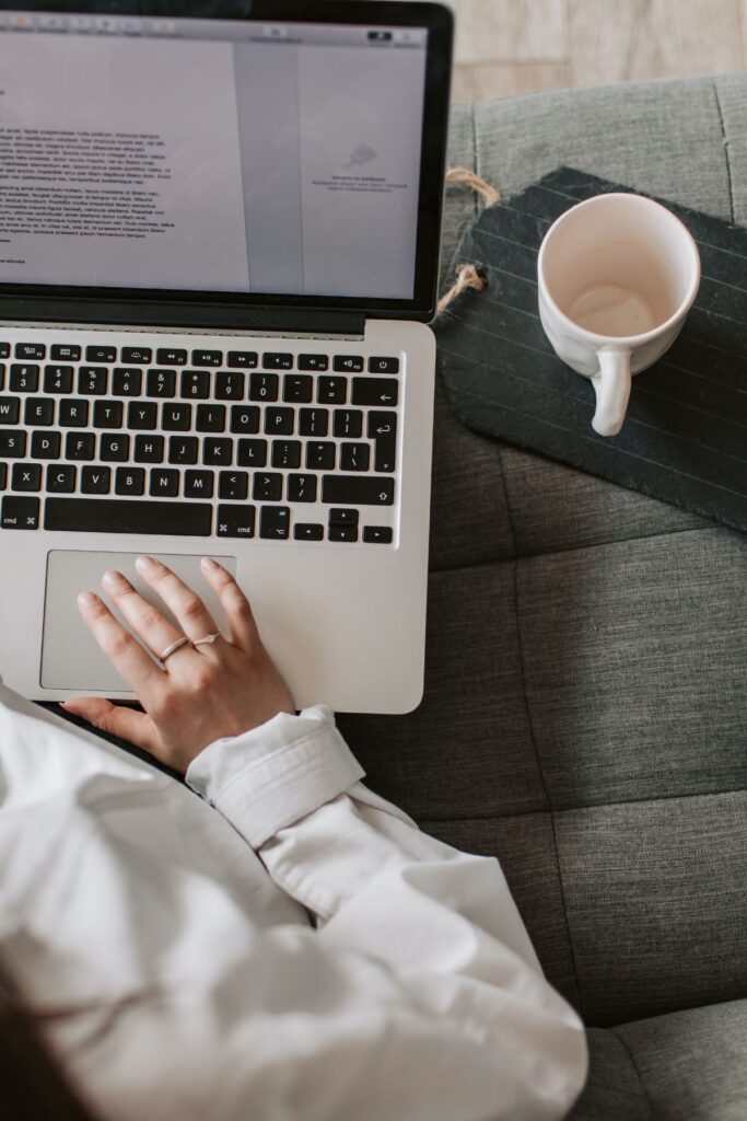 b97c758eed8a8a417ab6c553be5c8656 Person using a laptop on a couch with an empty coffee mug nearby. | Sky Rye Design Person using a laptop on a couch with an empty coffee mug nearby.