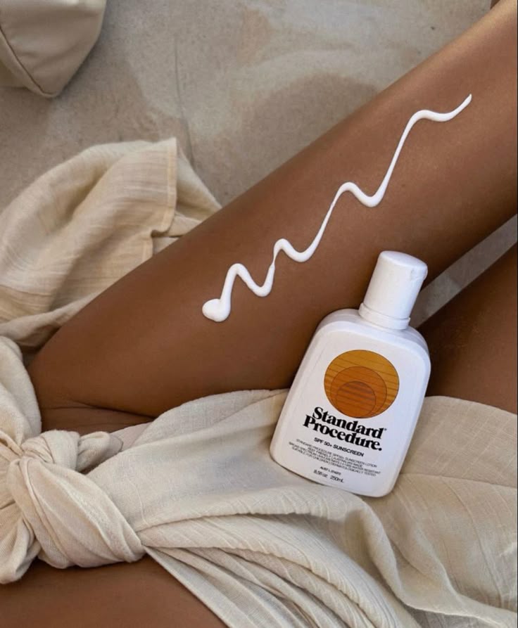 Bottle of sunscreen next to a white lotion line on tanned skin, wrapped in beige fabric, promoting sun protection.