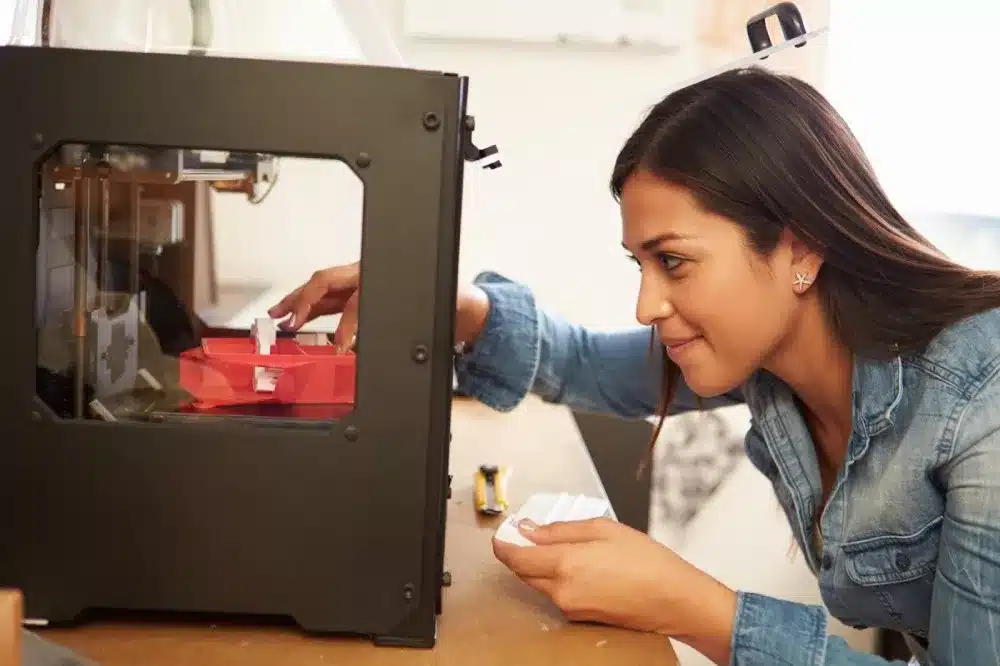 Woman using a 3D printer, adjusting model in a creative workspace.