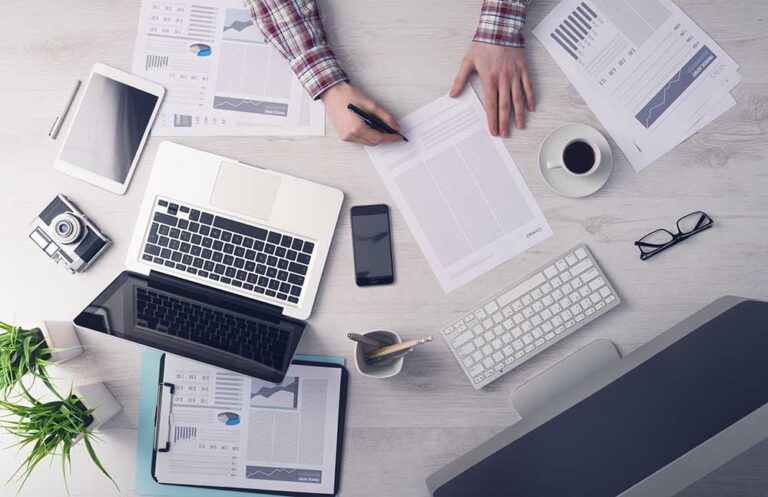 businesswriting Overhead view of modern workspace with laptop, tablet, charts, and coffee, emphasizing productivity and analysis. | Sky Rye Design Overhead view of modern workspace with laptop, tablet, charts, and coffee, emphasizing productivity and analysis.