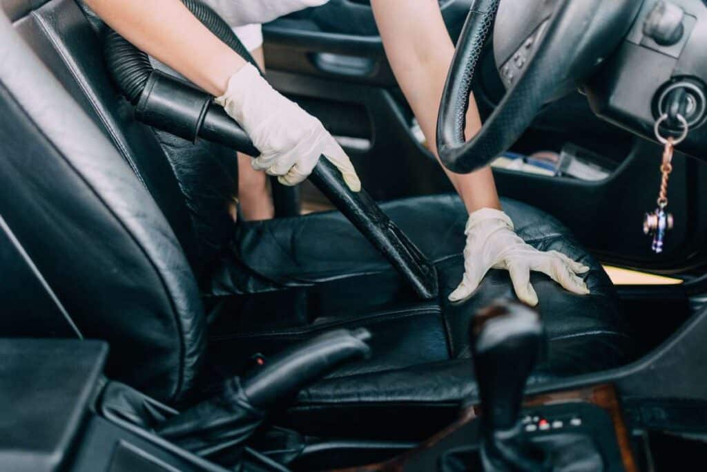 Person vacuuming car seat interior with gloves for deep cleaning.