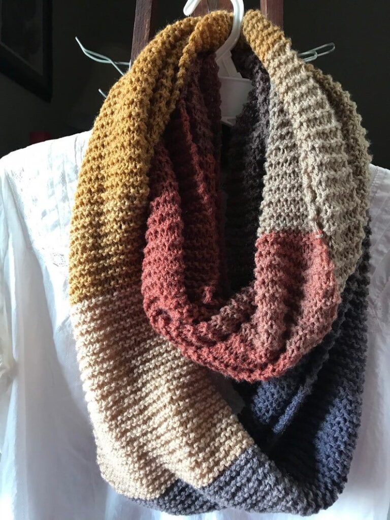 Cozy multicolored knit scarf hanging on a white hanger against a dark background.
