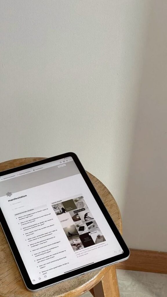 Tablet on wooden stool displaying a manifestation guide webpage, set against a minimalist beige wall.