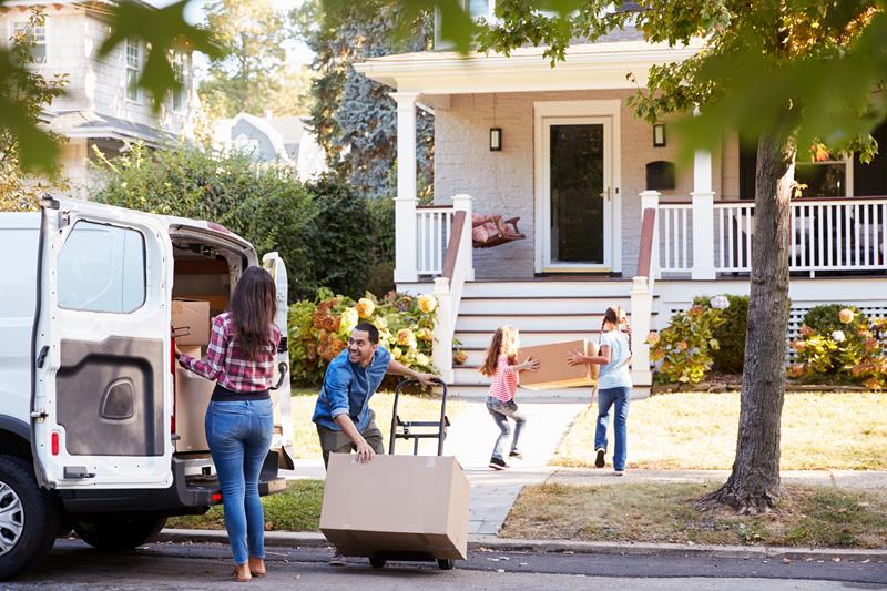 Family unloading boxes from a van in front of a house, symbolizing moving day.