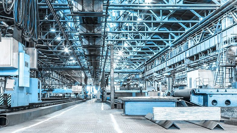 Spacious industrial warehouse with machinery and blue steel beams, well-lit and organized for manufacturing.