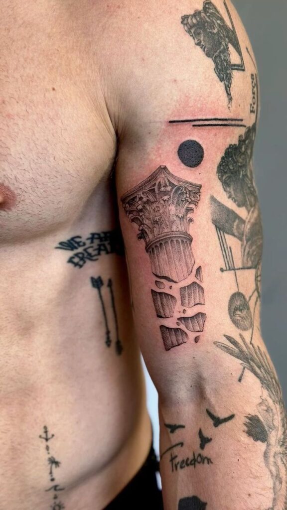 Arm tattoo featuring a detailed broken column design, surrounded by various black ink symbols and words.