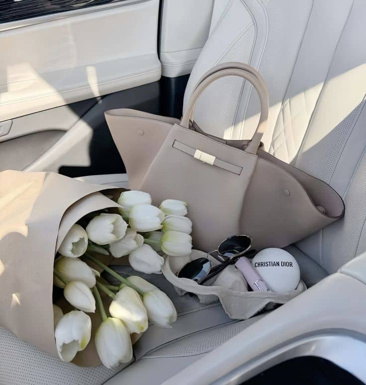 Beige handbag with white tulips and sunglasses on car seat, elegant luxury style accessory.
