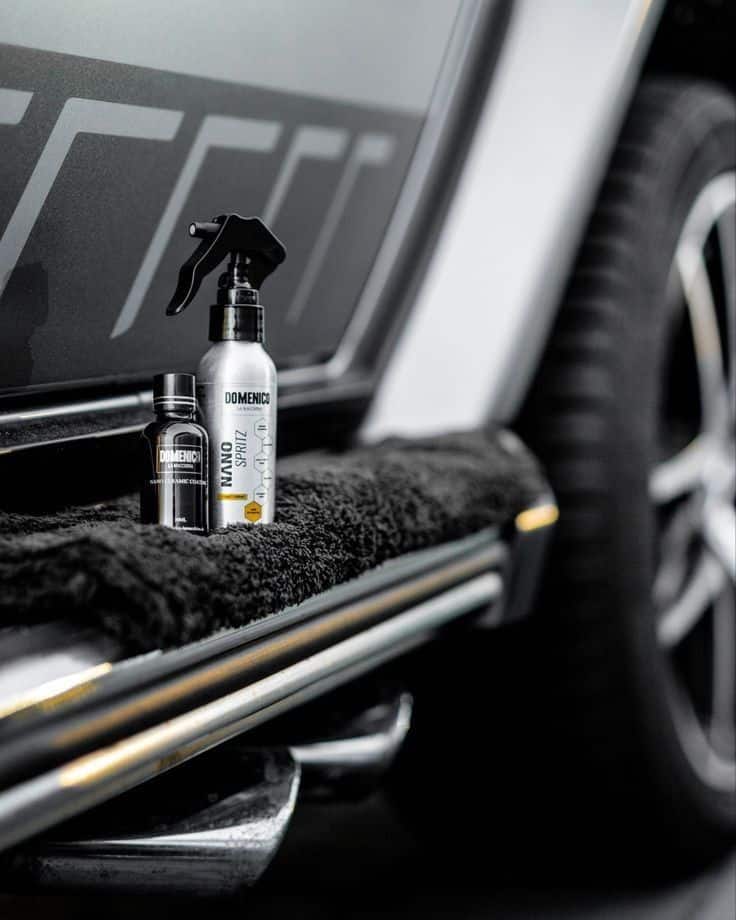 Car detailing products on black mat beside vehicle, showcasing automotive care essentials.