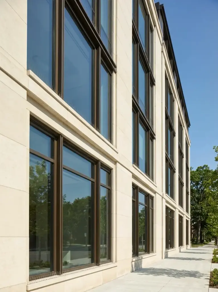 72436359-7513-4fc2-8b13-796db213a74f Modern limestone office building facade with large dark-framed windows reflecting trees and sidewalk | Sky Rye Design Modern limestone office building facade with large dark-framed windows reflecting trees and sidewalk