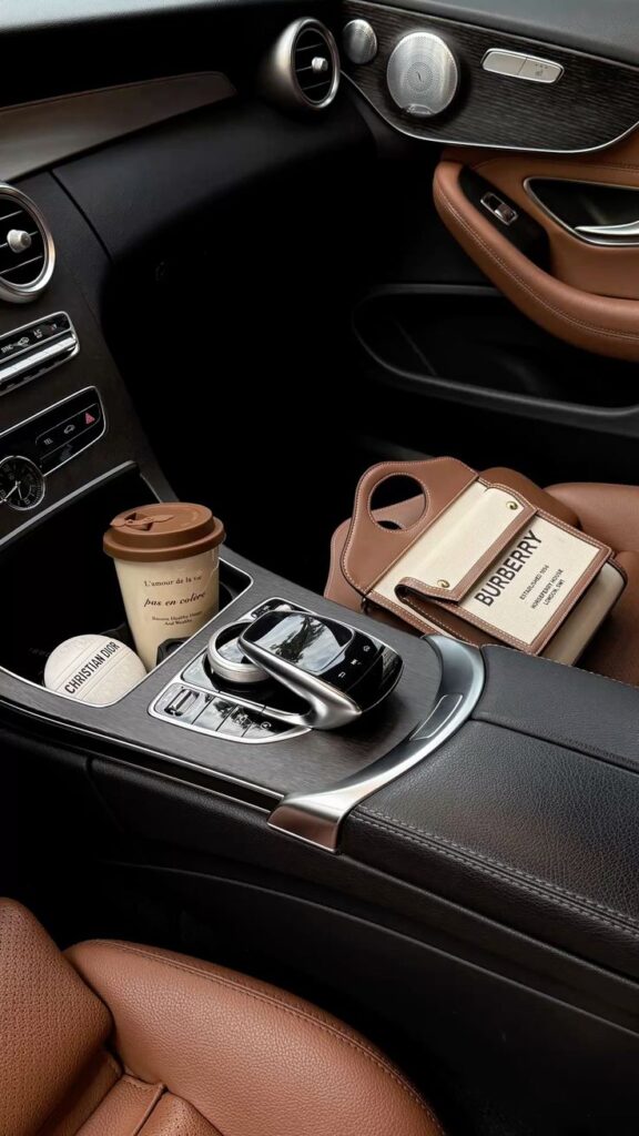 Luxury car interior with brown leather seats, coffee cup, and designer bag on the console.