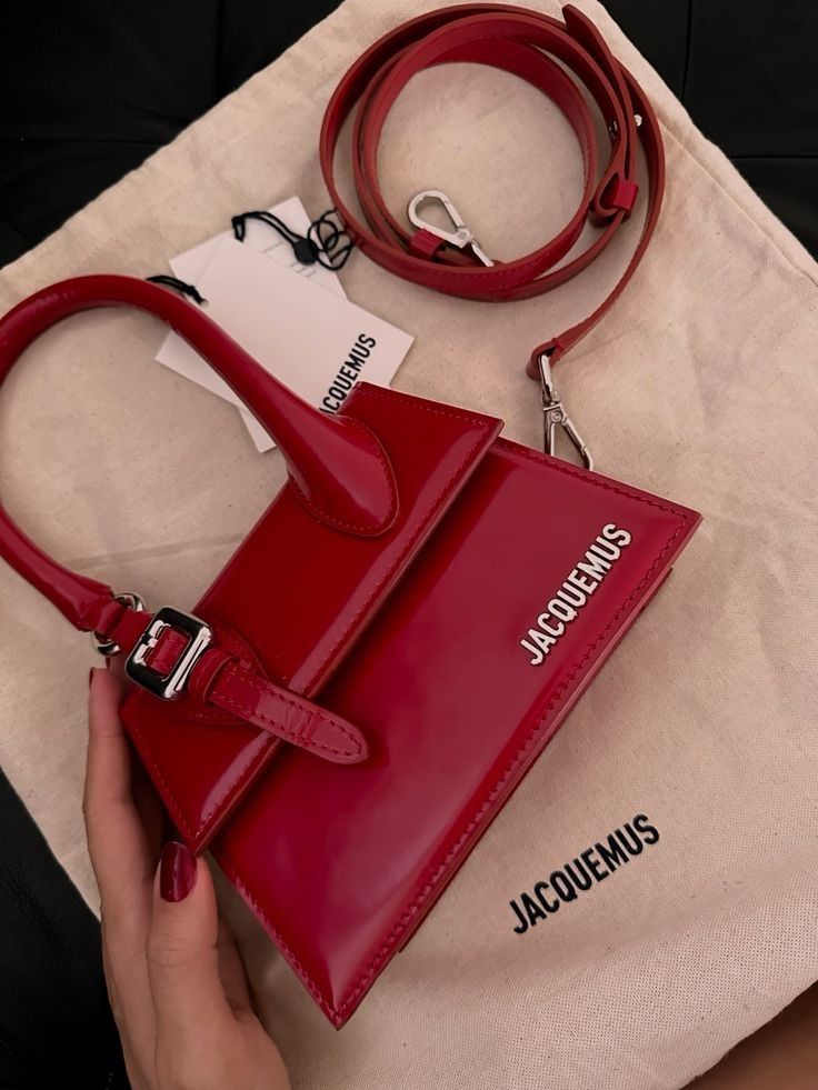 Red designer handbag with Jacquemus branding on a beige dust bag, includes a long matching strap.