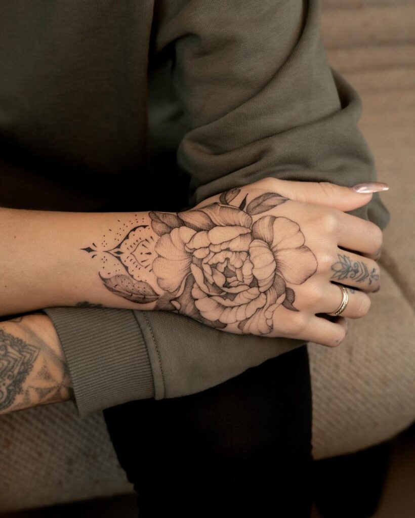 Close-up of a delicate floral hand tattoo with intricate shading, person wearing a cozy sweater, elegant manicure.