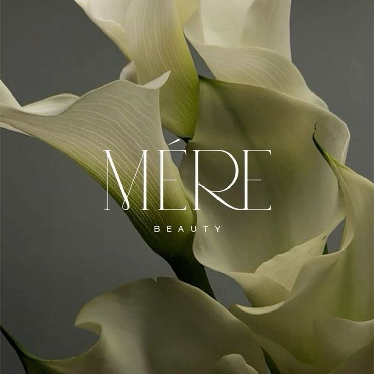 Elegant calla lilies with MÉRE Beauty text overlay on a muted gray background.