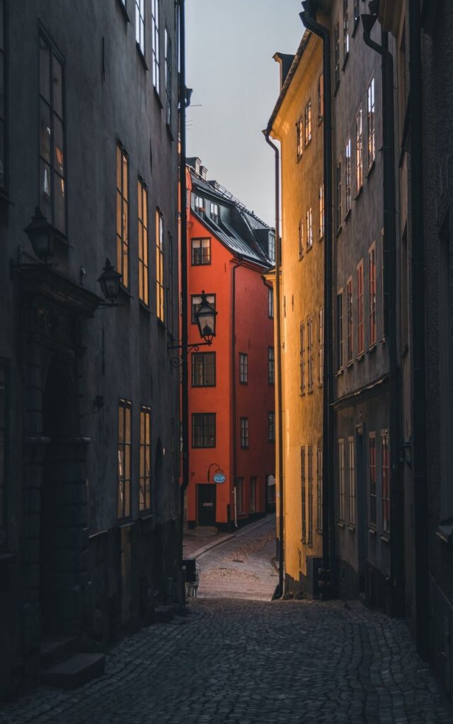 Narrow European street with cobblestones, surrounded by tall, colorful buildings in warm evening light.
