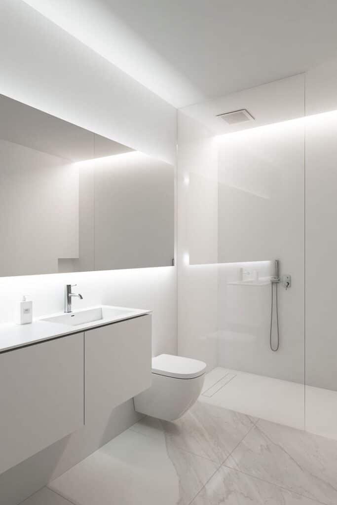 Minimalist white bathroom with sleek vanity, toilet, and modern shower area featuring ambient lighting.