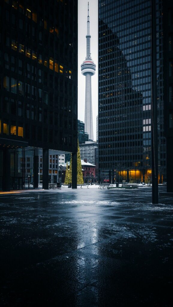 CN Tower framed by urban buildings on a snowy evening in Toronto, with holiday lights visible below.