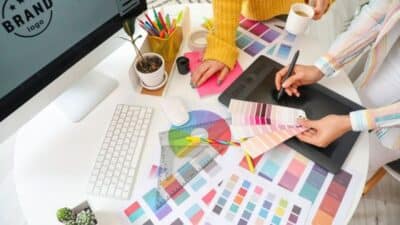 Designers selecting color swatches at a workspace with computer and tablet for branding project.