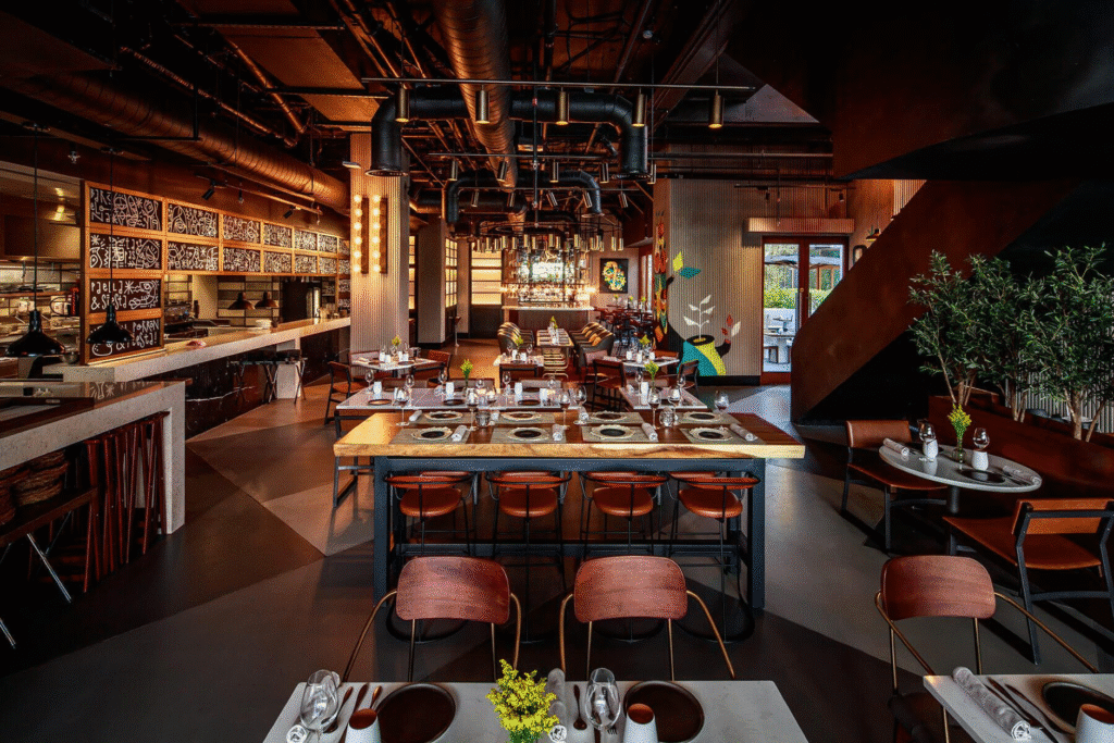 Modern restaurant interior with elegant decor, wood tables set for dining, and ambient lighting.