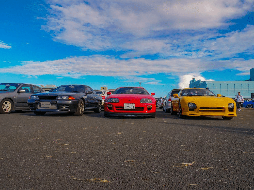 Lineup of classic sports cars under a blue sky at a car meet.