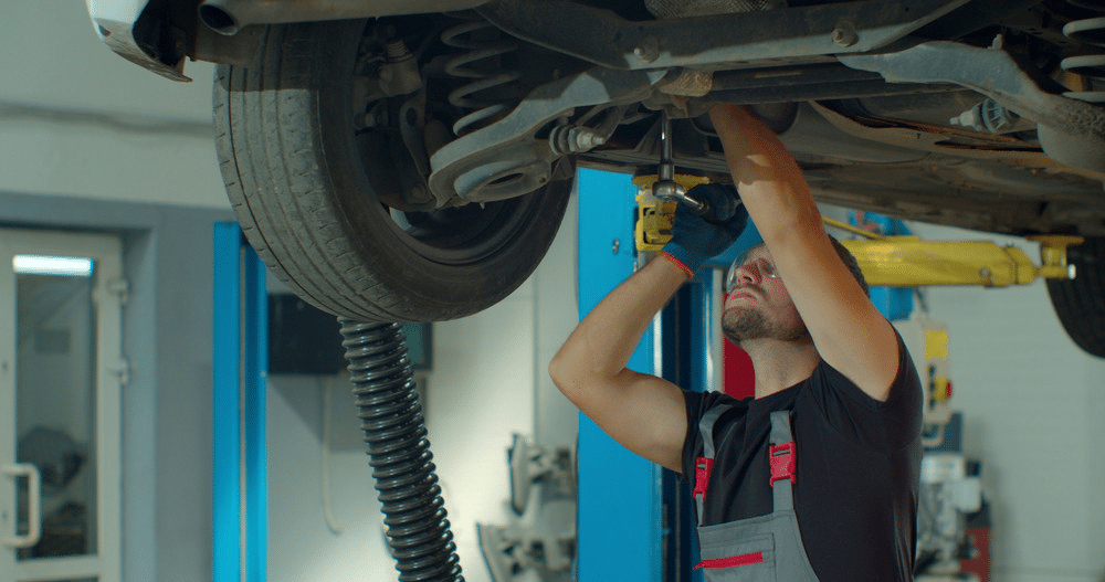Mechanic repairing car underside in workshop, using tools for maintenance.