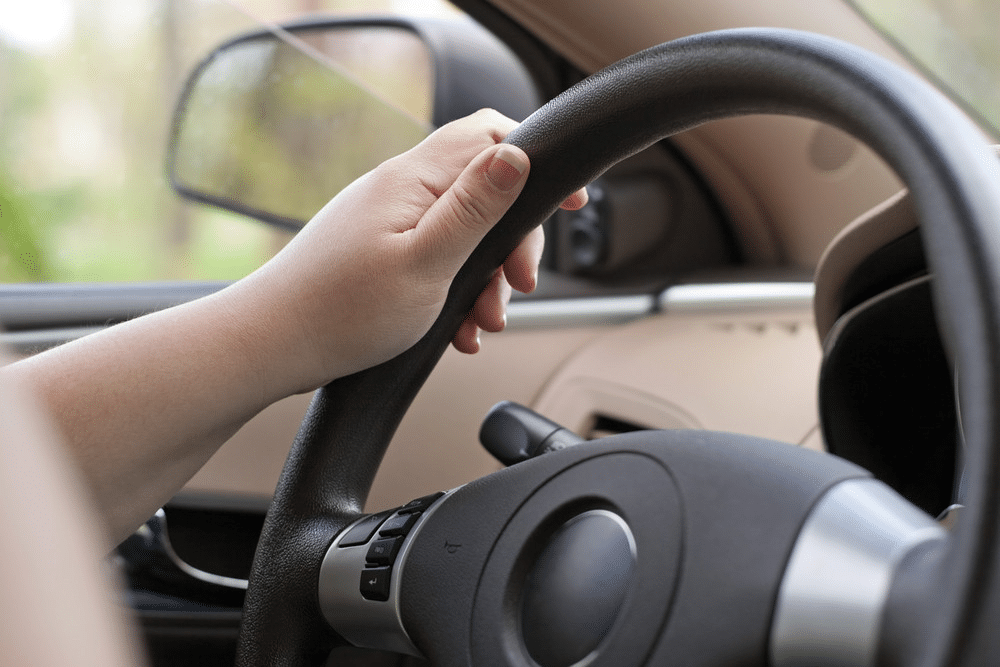 Close-up of a hand gripping a car steering wheel, emphasizing safe driving and control.