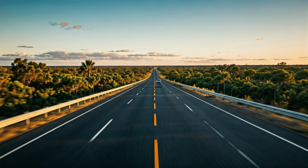 Open highway at sunset, surrounded by green trees under a clear blue sky with a few clouds.