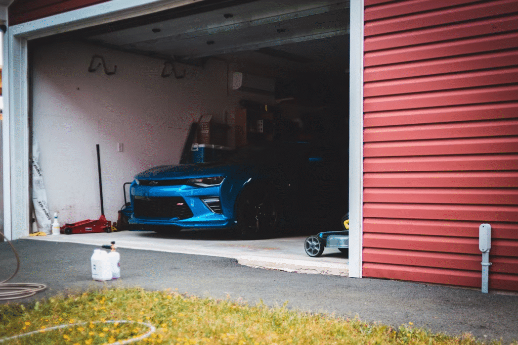 image2 Blue sports car parked in a garage, partially visible with a red door, surrounded by tools and containers. | Sky Rye Design Blue sports car parked in a garage, partially visible with a red door, surrounded by tools and containers.