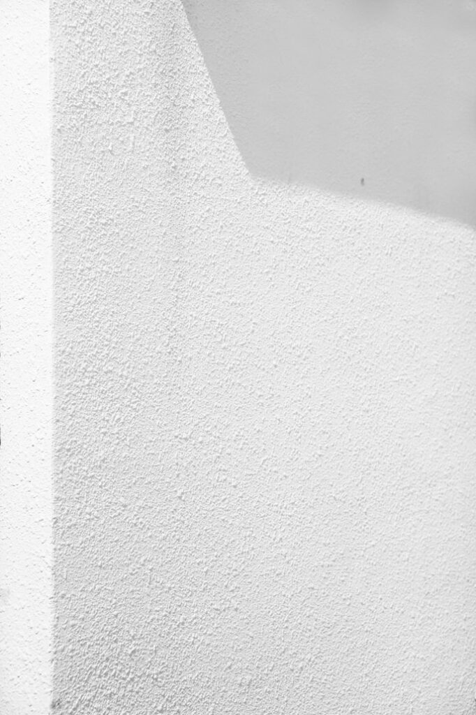 Close-up of textured white stucco wall with sharp shadows, showcasing minimalist architectural design elements.