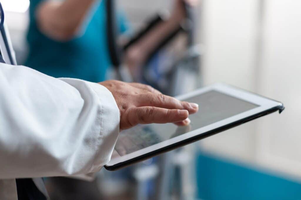 Doctor in white coat using a tablet for medical data entry in a hospital setting.