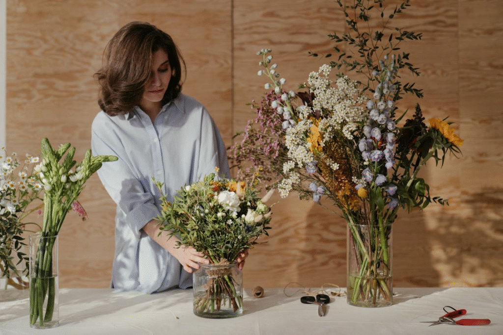 Woman arranging colorful floral bouquet in glass vase on table with scissors nearby.