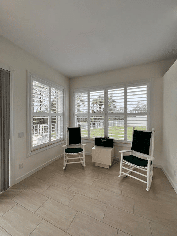 Bright sunroom with two chairs, large windows with shutters, and scenic garden view.