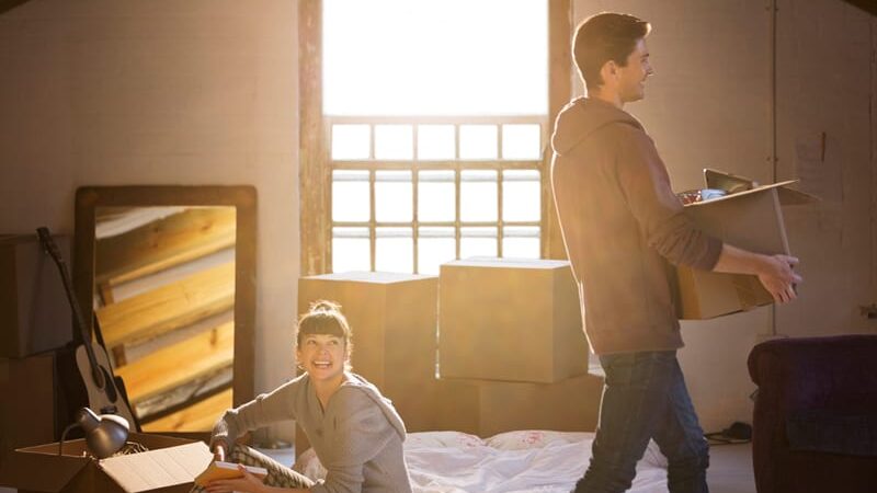 Young couple unpacking boxes in sunny room, smiling and setting up their new home.