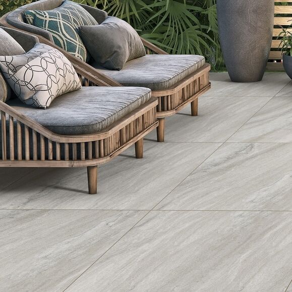 Outdoor seating with gray cushions on stylish lounge chairs, set on a tiled patio with lush greenery in the background.