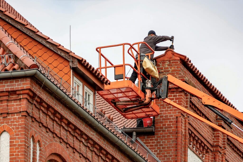 pexels-guvo59-31762405 Worker on cherry picker repairing brick chimney on tile-roofed building. | Sky Rye Design Worker on cherry picker repairing brick chimney on tile-roofed building.