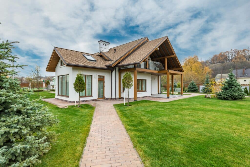 Modern suburban house with a lush green lawn, surrounded by trees under a cloudy sky.