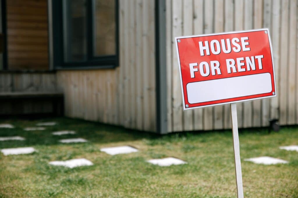 House for rent sign in front yard, wooden siding background.