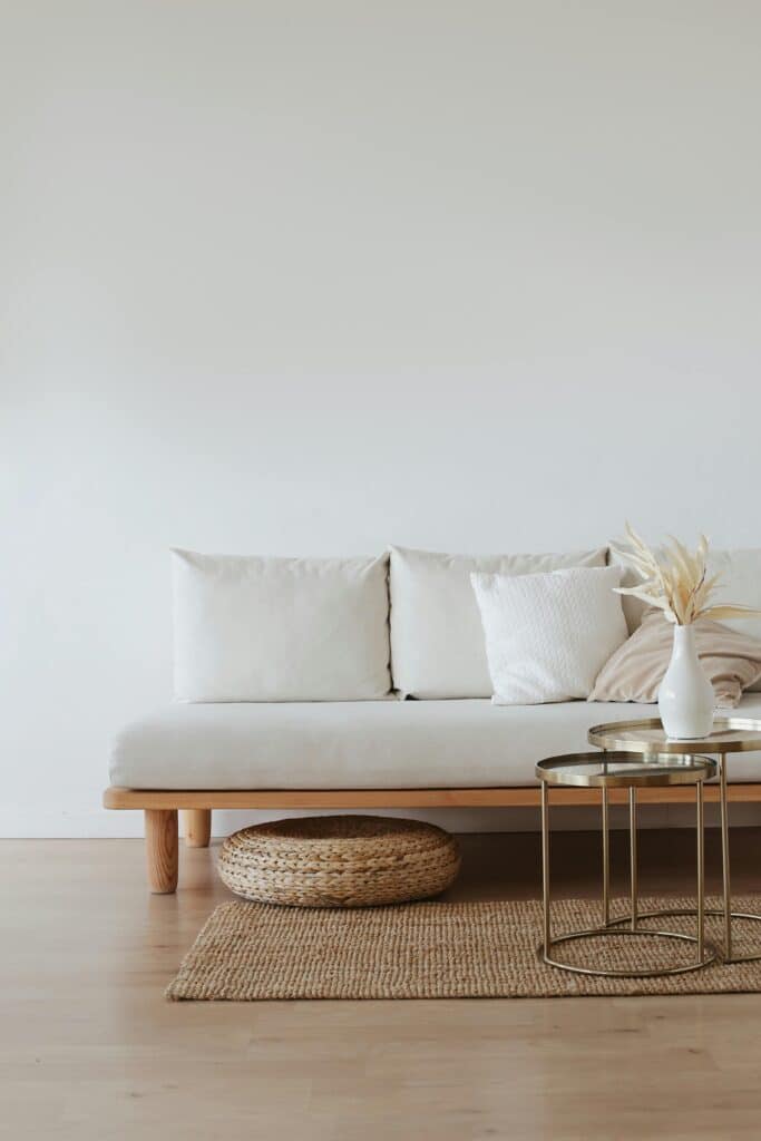 Minimalist living room with a white sofa, decorative pillows, woven rug, and elegant side tables with a vase.